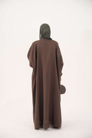 Back view of a brown bisht abaya with loose elegant cut, worn with a dark green hijab and holding a small handbag