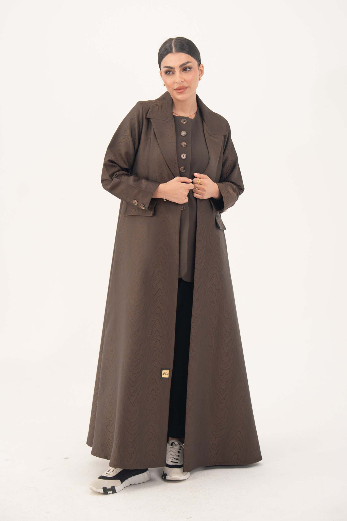Woman wearing a brown jacquard blazer abaya with sharp lapels, structured tailoring, and faux pockets, styled for formal and professional looks.