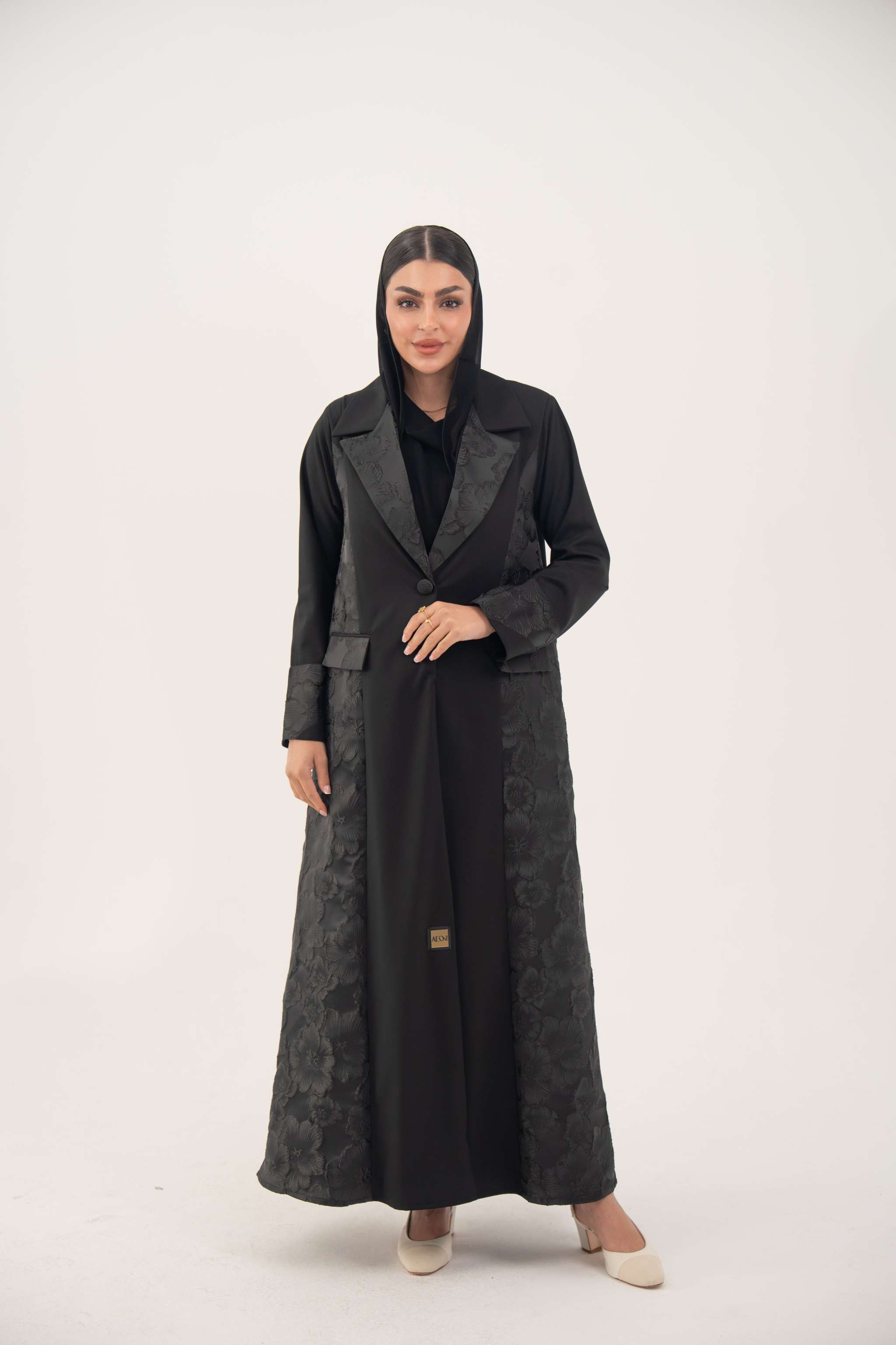 Woman wearing a black jacquard blazer abaya with a textured pattern and classic lapels, featuring a tailored and elegant silhouette.