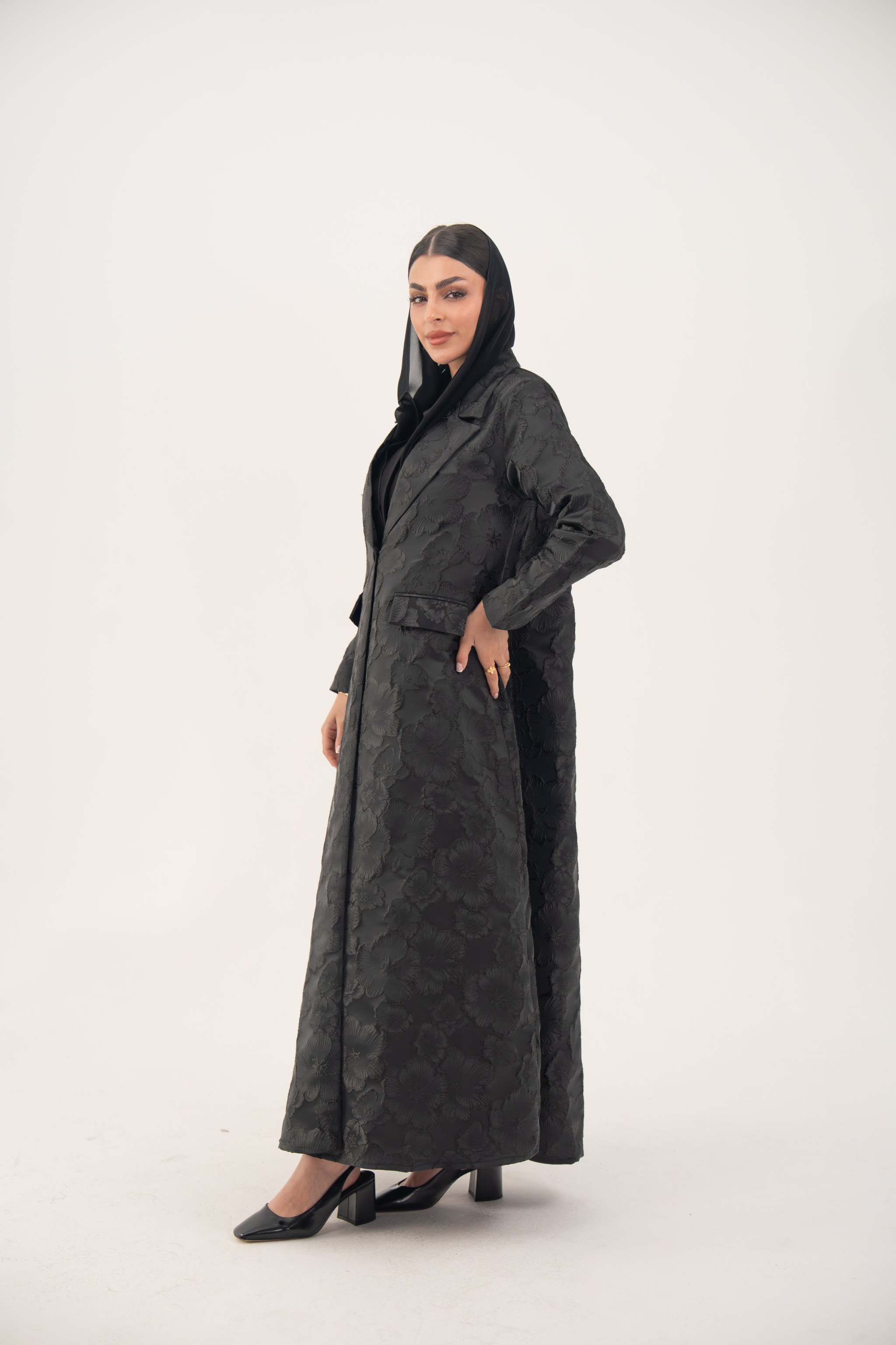 Woman wearing a black jacquard blazer abaya with textured pattern and classic lapels, styled for formal occasions.