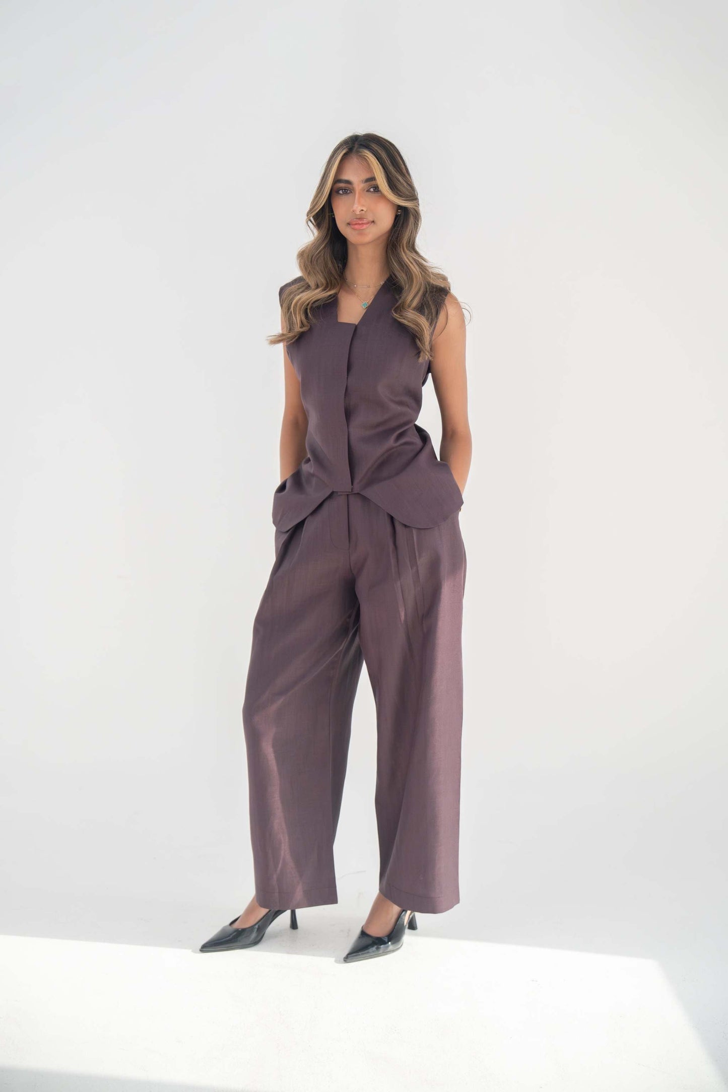Woman wearing relaxed fit Ube Pant in deep purplish-brown twill linen blend paired with sleeveless top and black heels