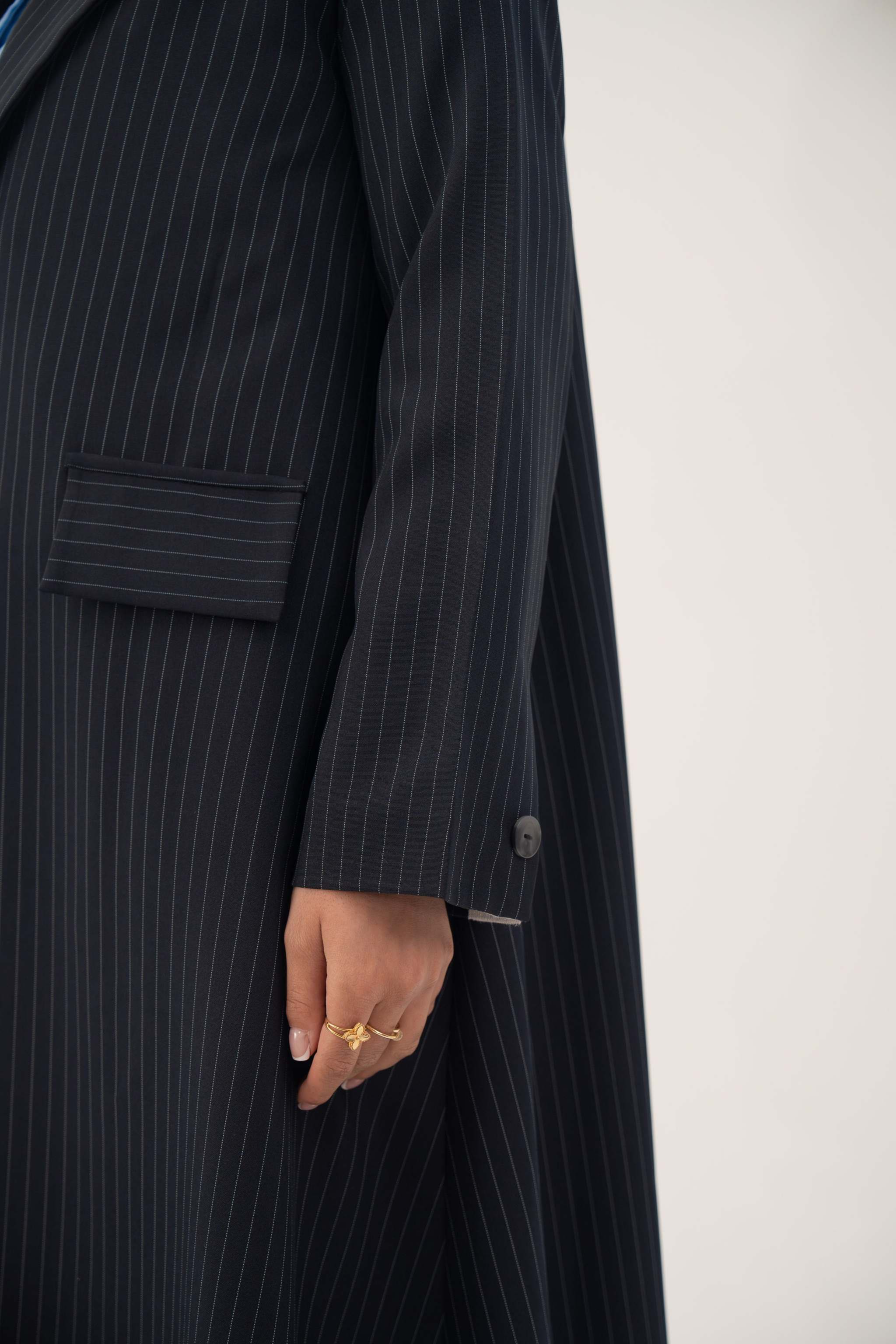 Deep navy crepe blazer with white pinstripes, wide lapel, shoulder pads, decorative pockets, and buttoned cuffs.