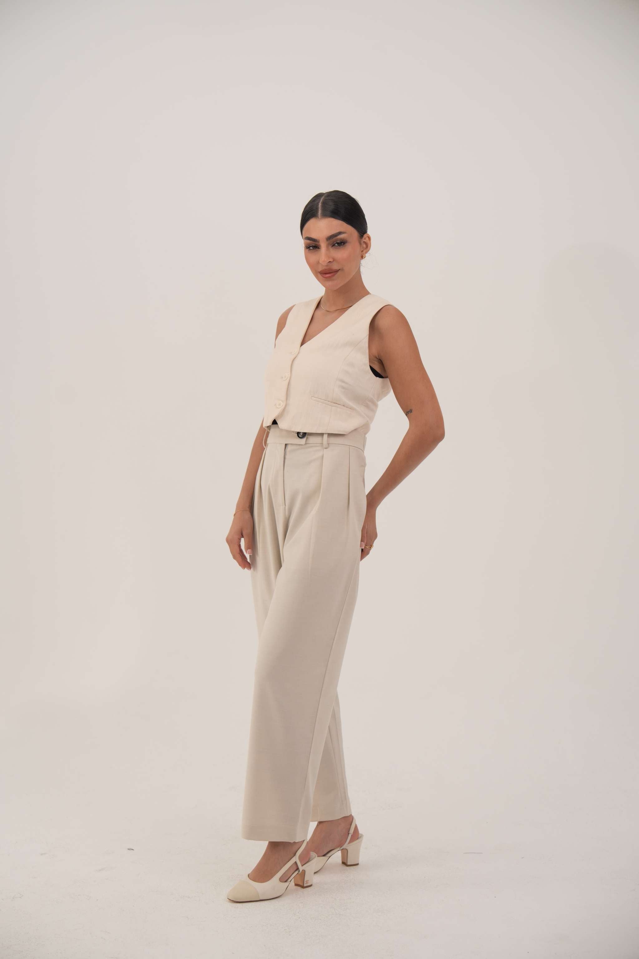 Woman wearing soft beige sleeveless crepe vest with front buttons and high-waisted beige pants