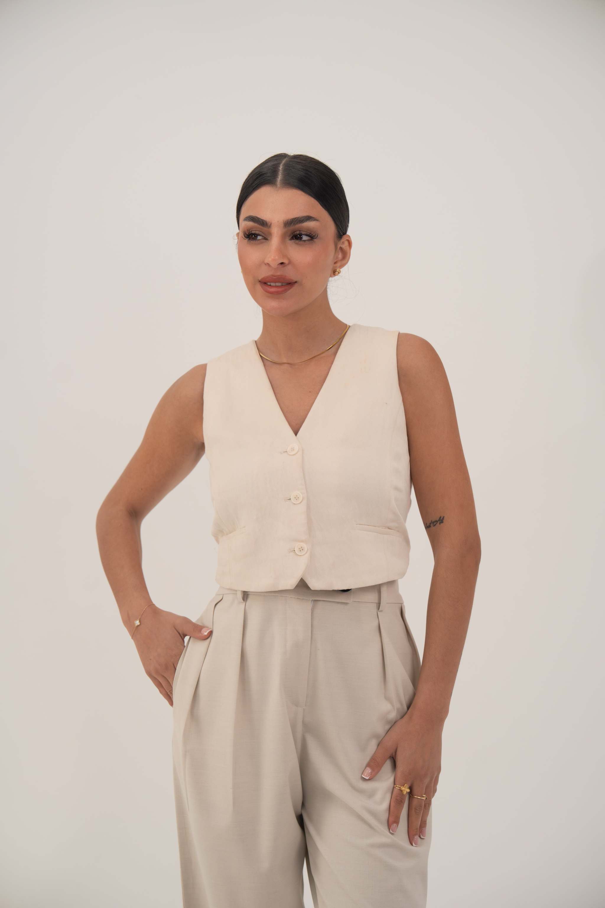 Woman wearing a soft beige sleeveless crepe vest with front button closure and light beige pants.