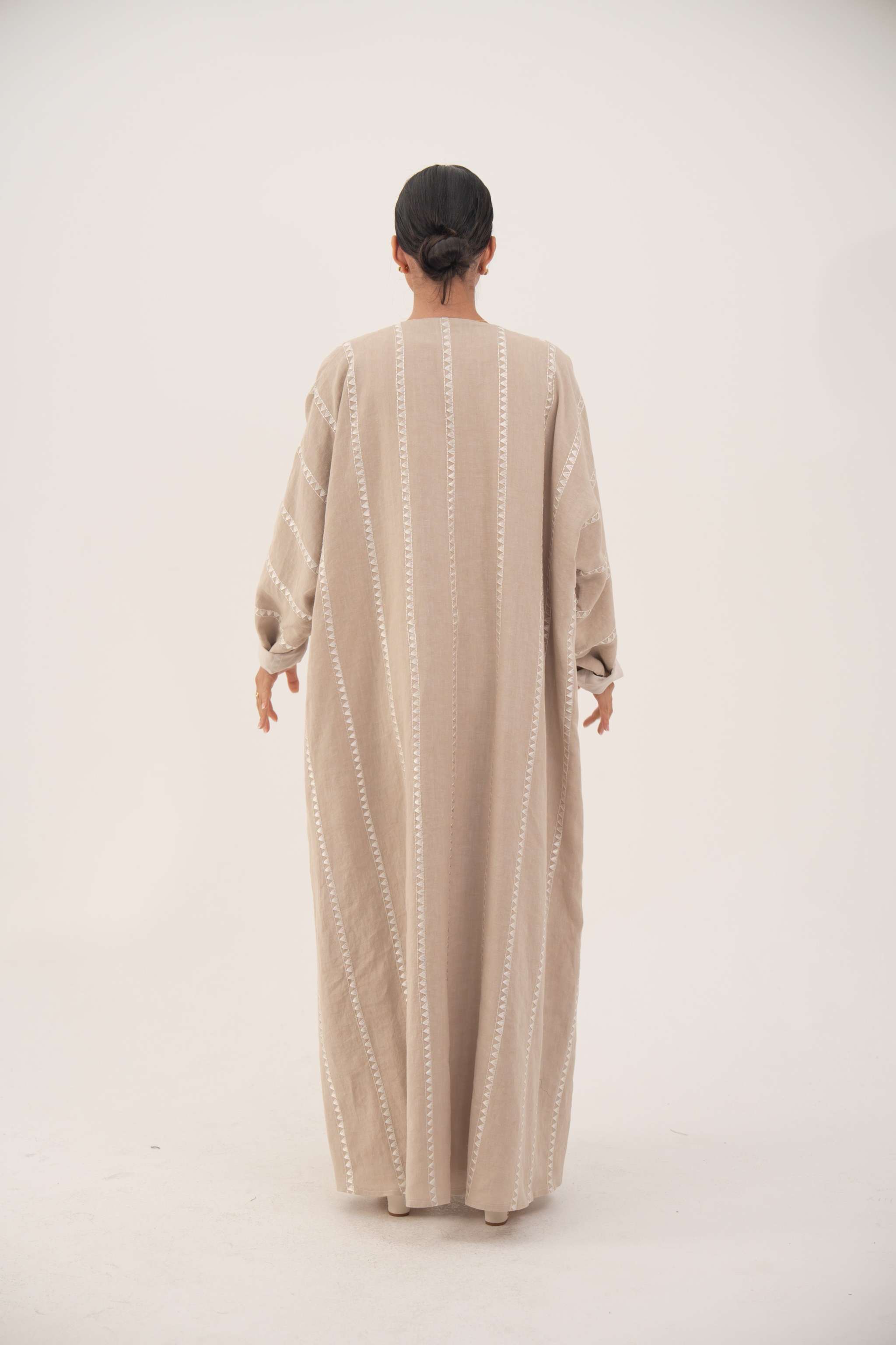 Back view of a creamy beige airy linen abaya with subtle tonal embroidery and soft chiffon cuffs, featuring a classic bisht silhouette and open front for graceful flow.