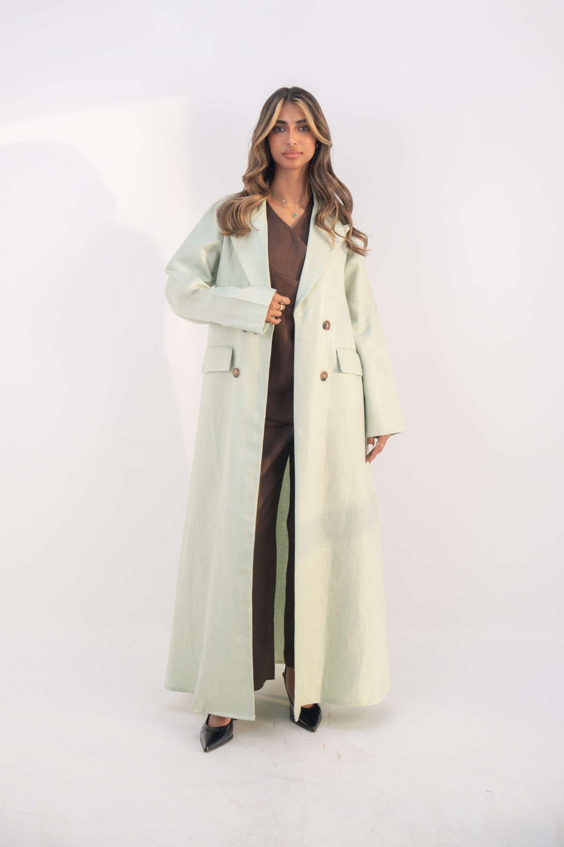 woman wearing mint green blazer abaya with structured lapels and statement buttons standing against white background