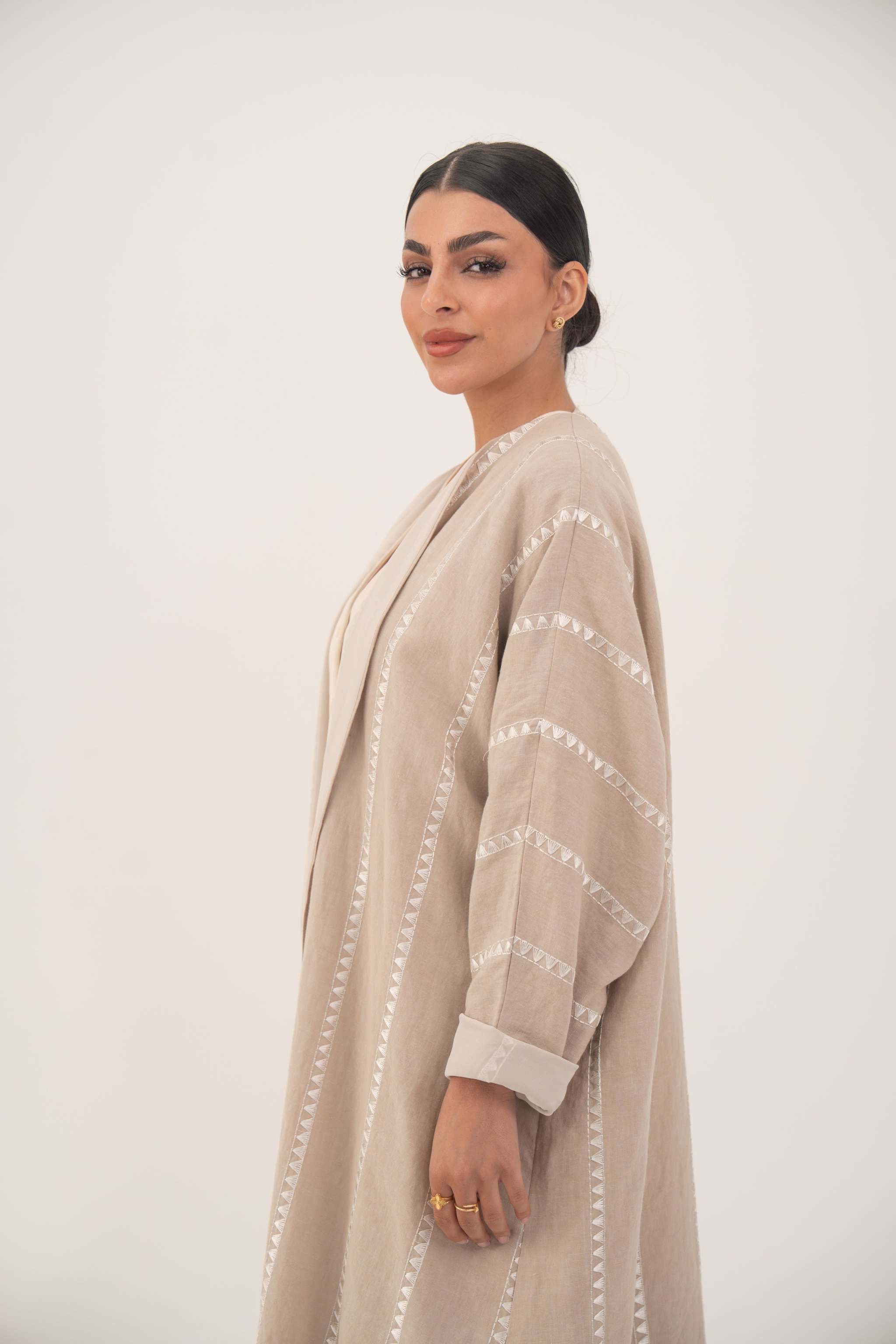 Woman wearing a creamy beige airy linen abaya with tonal embroidery and soft chiffon cuffs in an open front bisht silhouette
