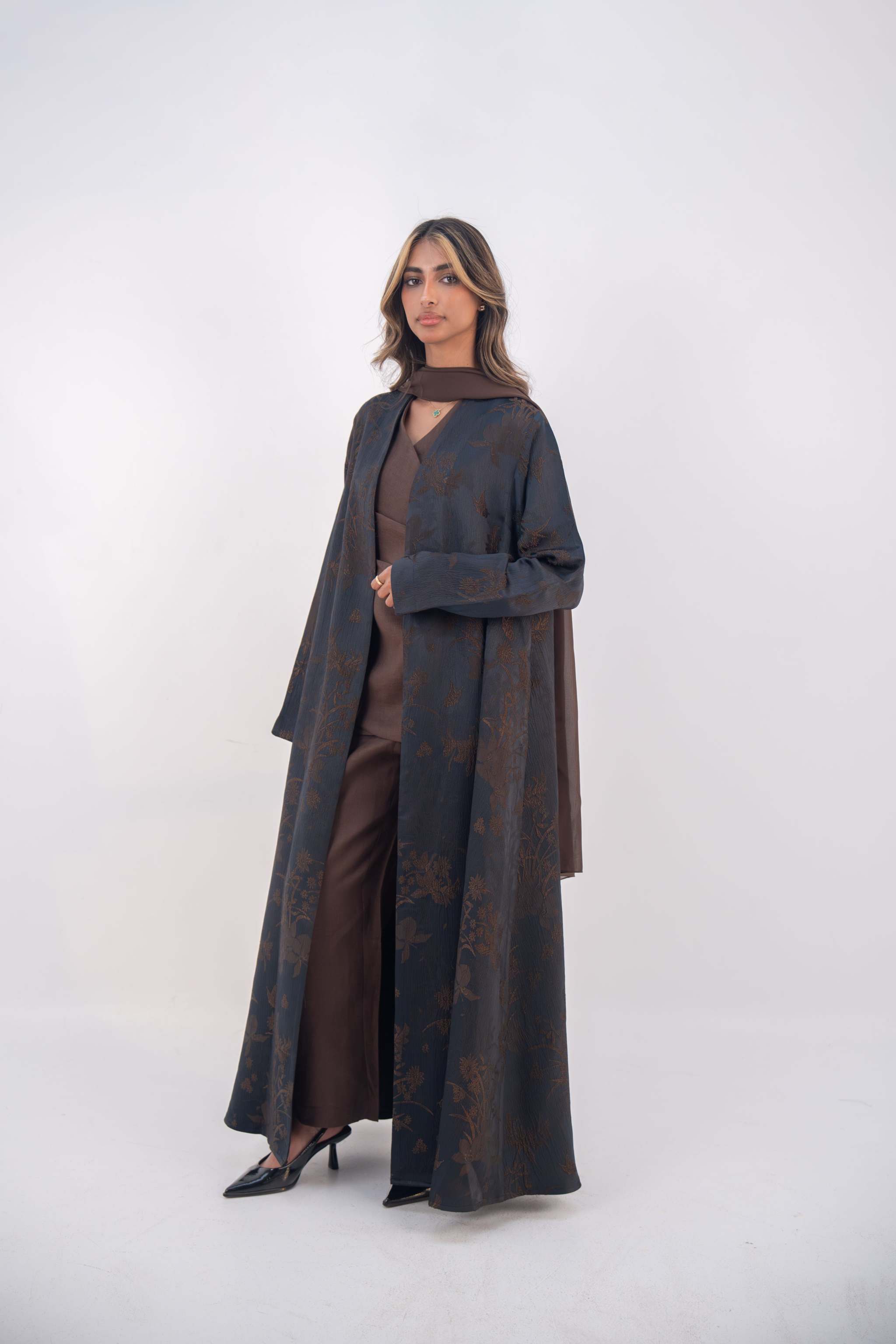 Woman wearing deep navy elegant jacquard silk abaya with subtle brown floral patterns and wide sleeves