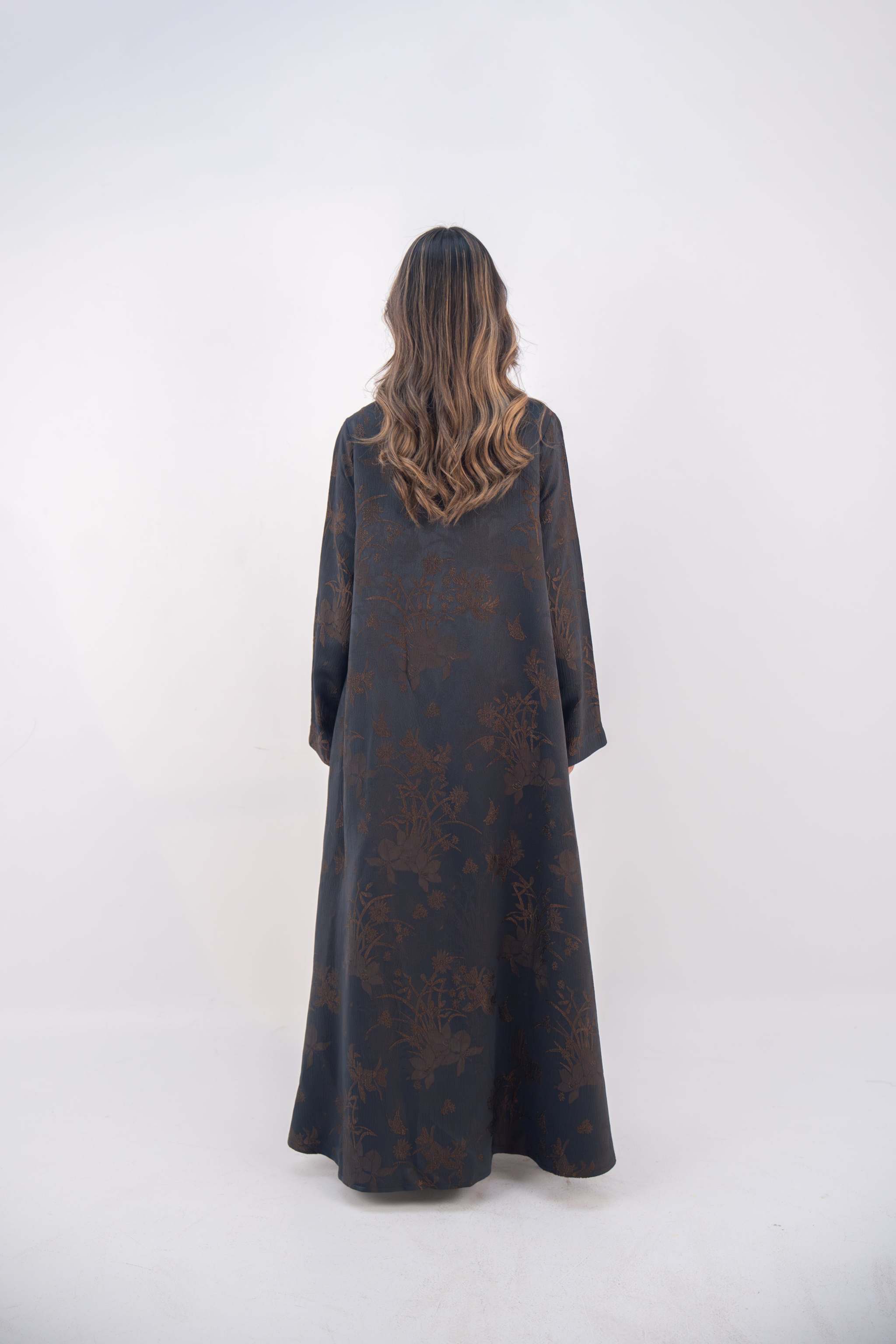 Back view of a navy jacquard silk abaya with subtle brown floral patterns and wide sleeves on a standing woman