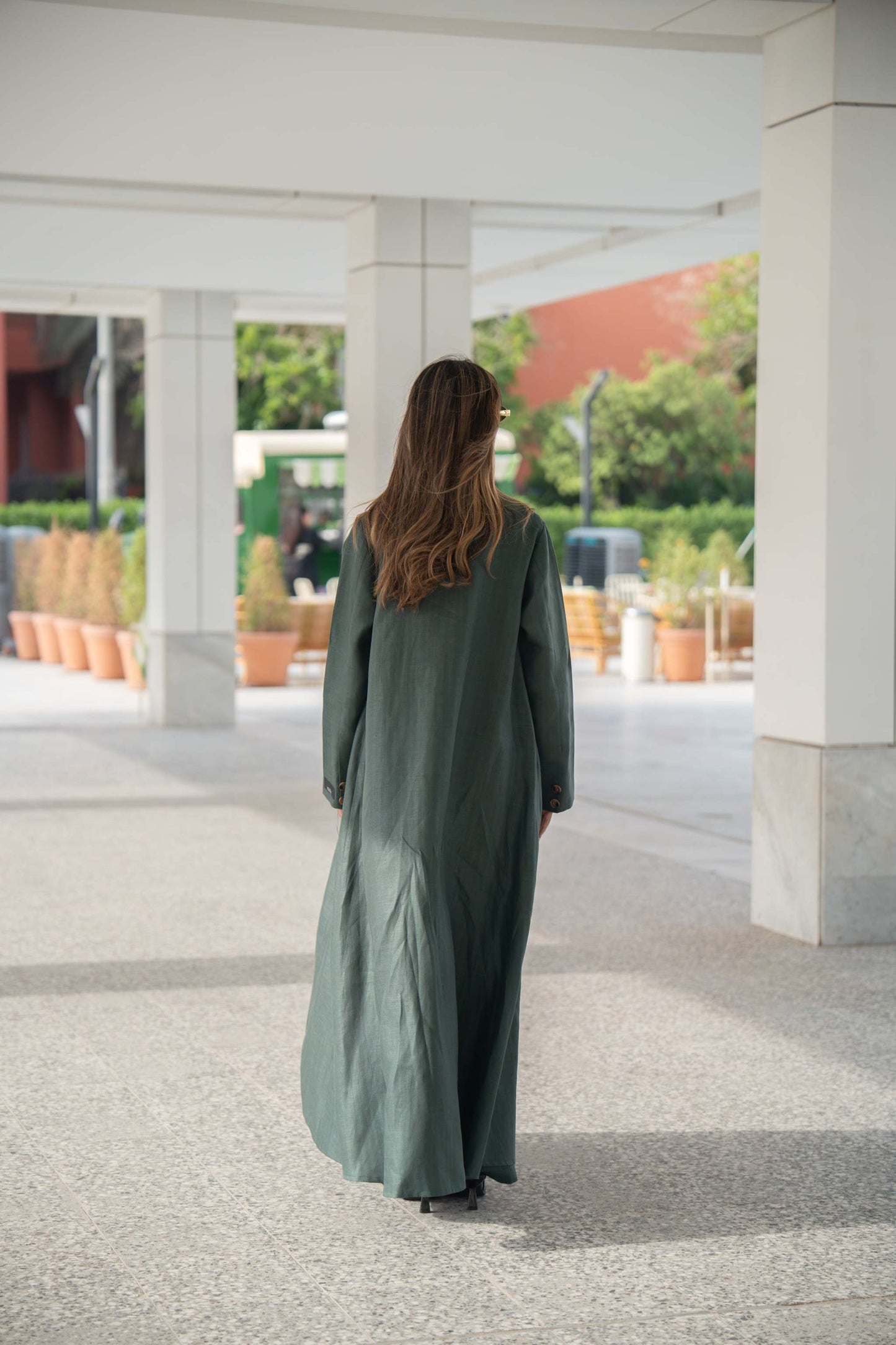 woman wearing dark green linen blazer abaya walking outdoors under white columns