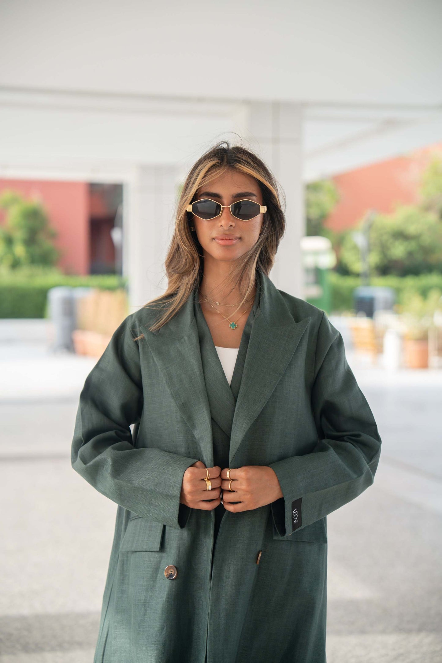 Woman wearing a dark green linen blazer with structured cut and brown trim on collar and edges