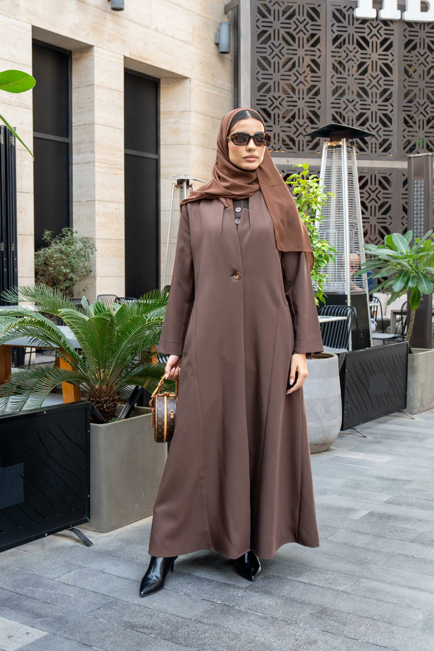 Woman wearing classic brown crepe abaya with hijab and sunglasses outdoors