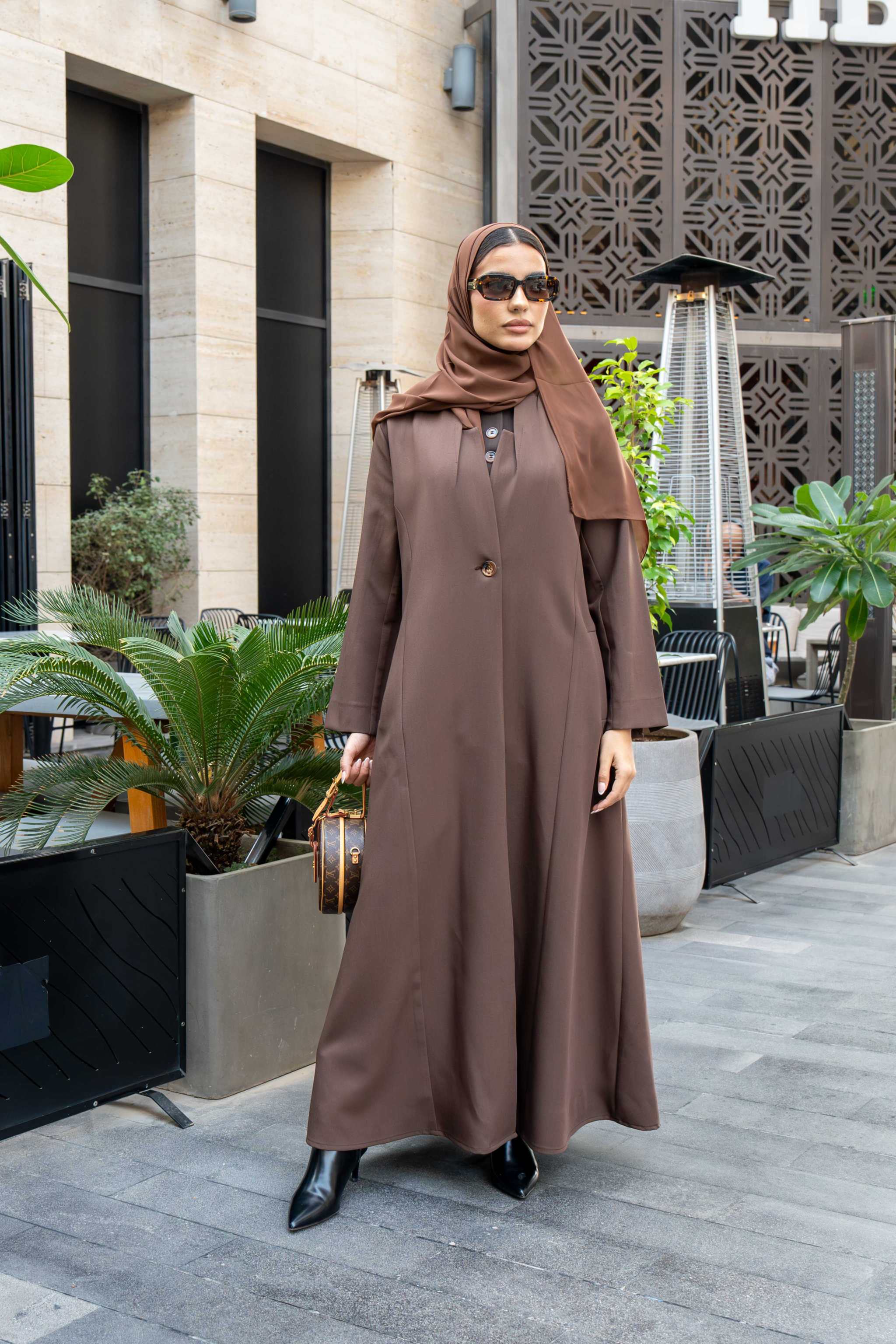 Woman wearing classic brown crepe abaya with hijab and sunglasses outdoors