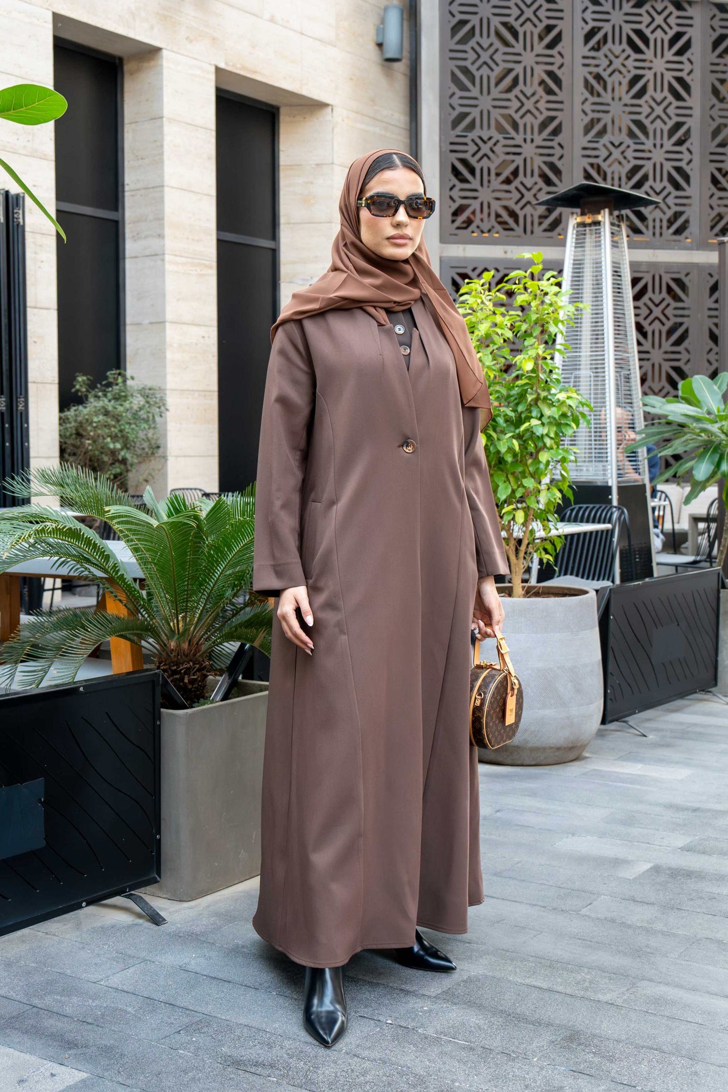 Woman wearing classic brown crepe abaya with hijab and sunglasses outdoors