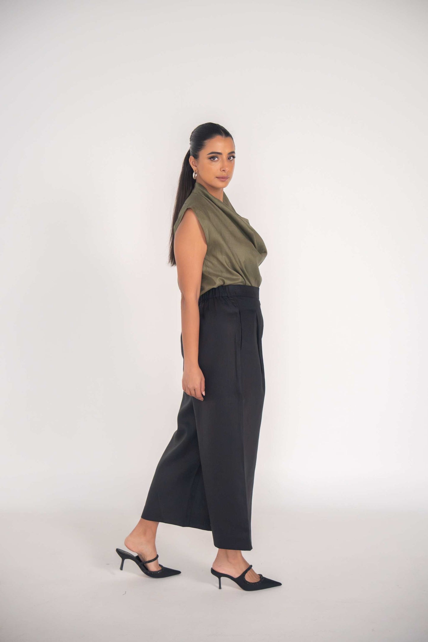 Woman wearing black Raya Pant with straight-leg cut and olive sleeveless top in studio setting