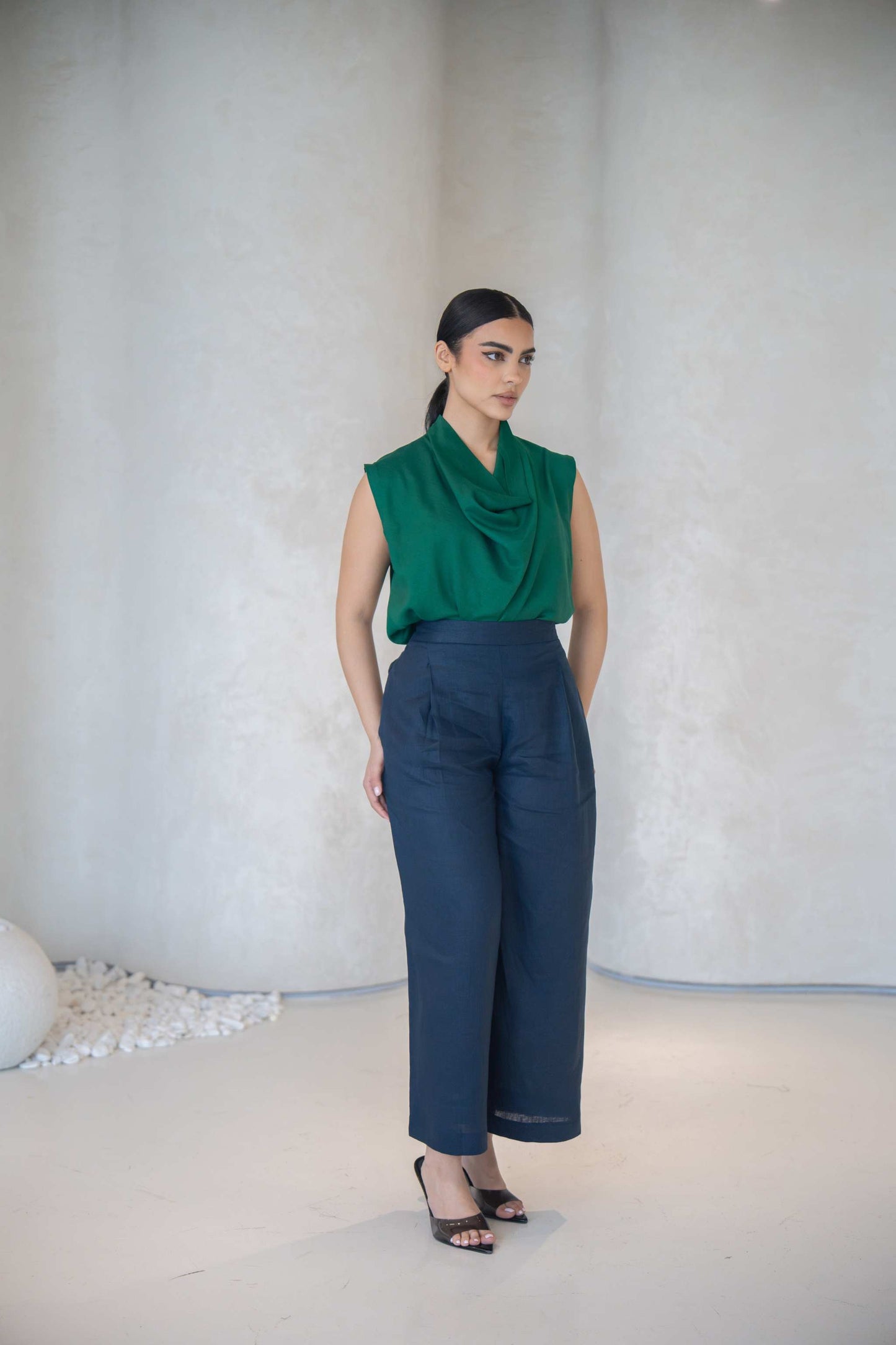 Woman wearing an emerald green sleeveless blouse with cowl neckline and navy wide-leg pants