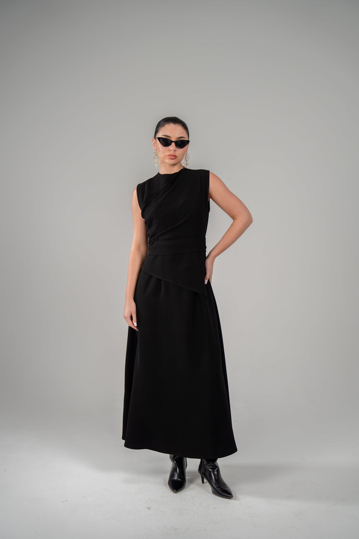 Woman wearing luxury black crepe dress with pleated neckline and matching belt against grey background