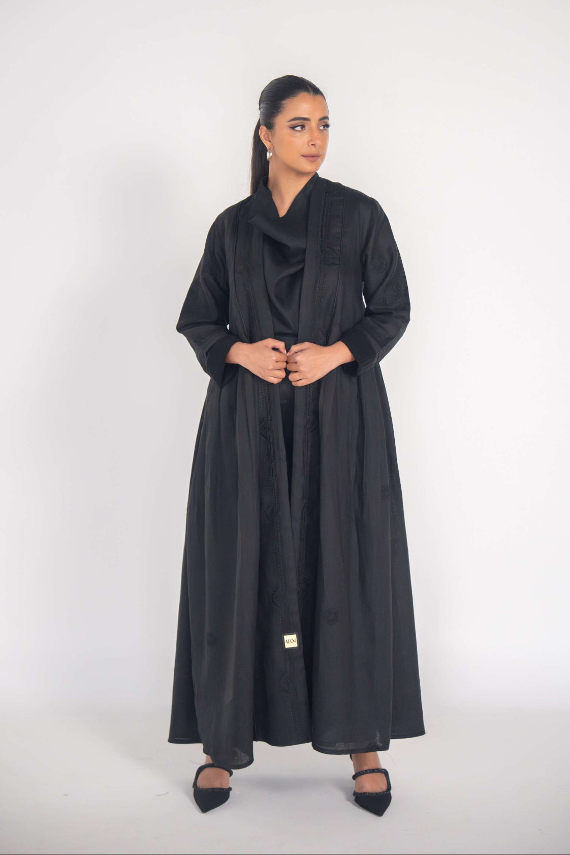 Elegant black refined abaya with breathable linen fabric, side pleats, and subtle black-on-black embroidery.