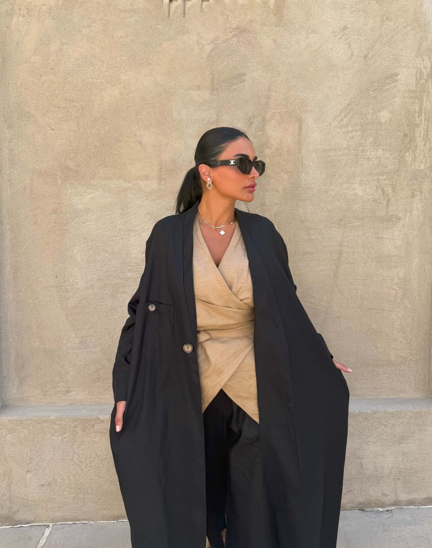 Woman wearing minimalist black linen abaya with straight cut and open front over beige outfit