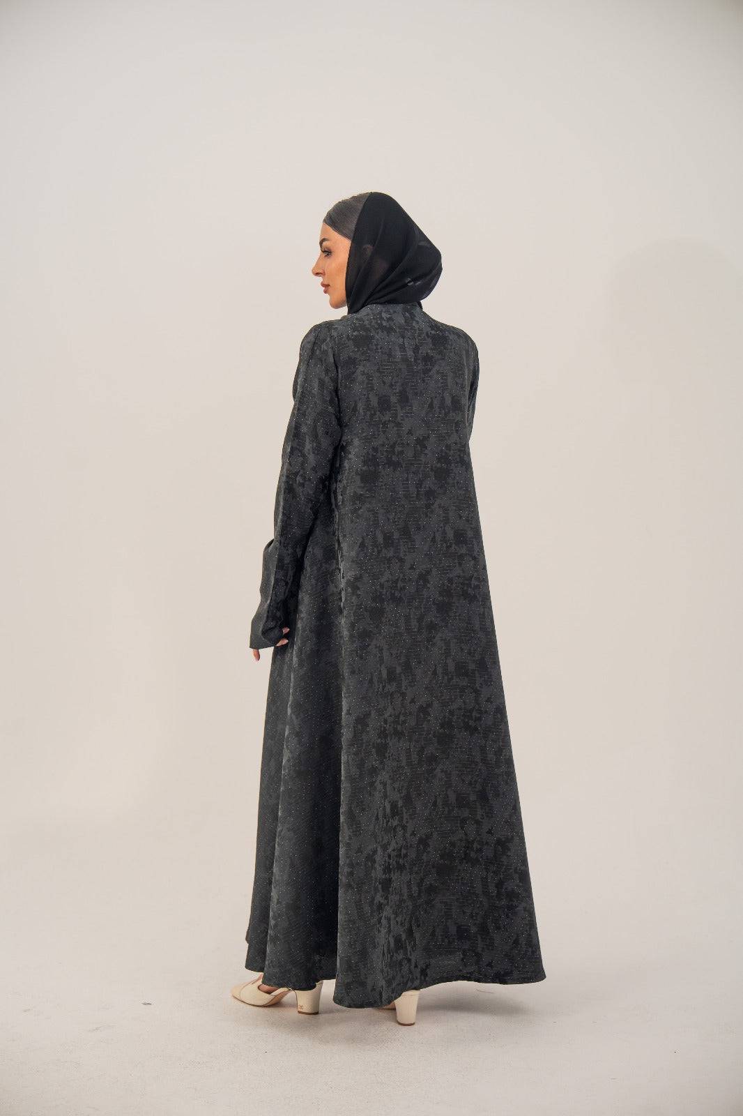 Woman wearing 'Ashmere' open-front black silk abaya with subtle abstract pattern and charcoal gray shimmer, viewed from back