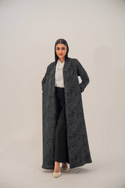Woman wearing an open-front black silk abaya with subtle abstract pattern and light shimmer, styled with white top and black pants.