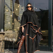 Woman wearing black leather-trimmed chamois poncho with brown knee-high boots and sunglasses outdoors - Leather Trace
