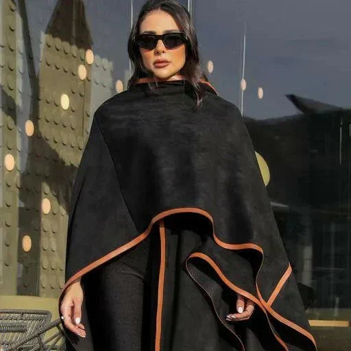 Woman wearing black leather-trimmed chamois poncho with brown knee-high boots and sunglasses outdoors - Leather Trace