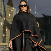 Woman wearing black leather-trimmed chamois poncho with brown knee-high boots and sunglasses outdoors - Leather Trace
