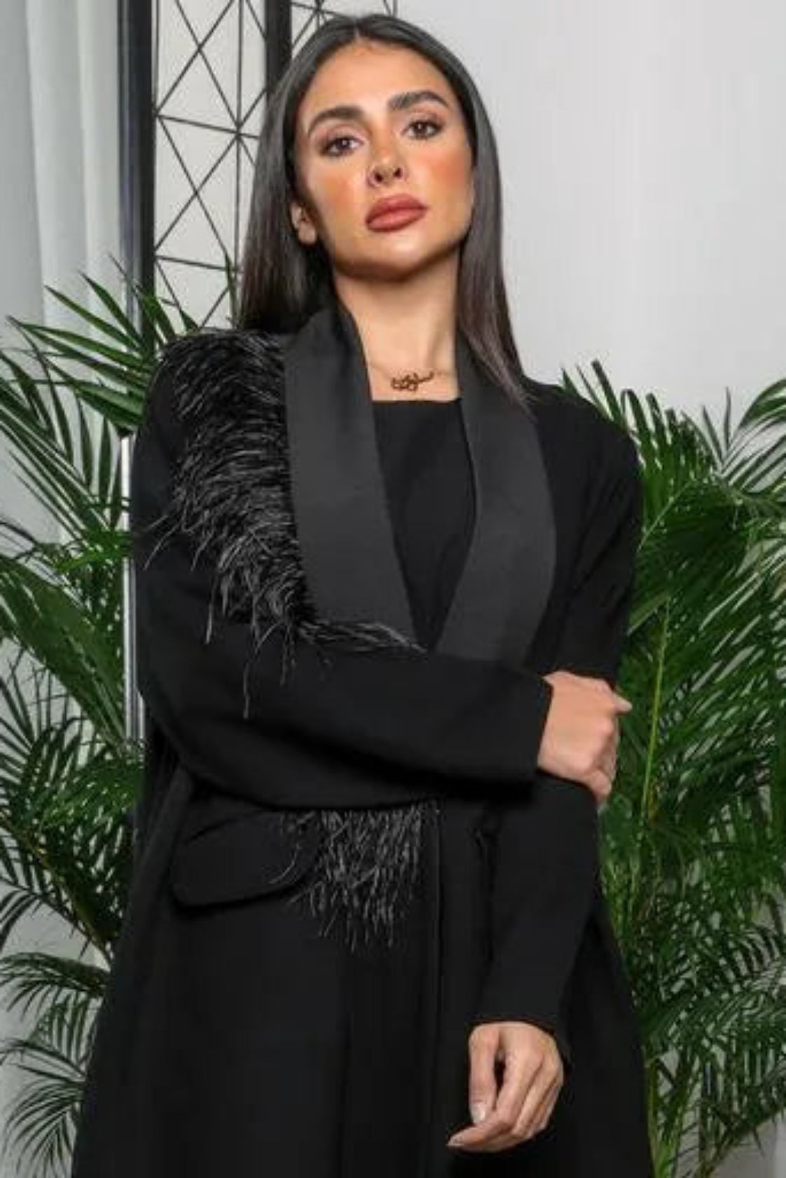 Woman wearing a black crepe blazer-style abaya with satin lapel and feather detailing on one shoulder.