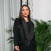 Woman wearing a black crepe blazer-style abaya with satin lapel and feather detailing on one shoulder.