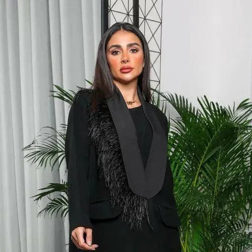 Woman wearing a black crepe blazer-style abaya with satin lapel and feather detailing on one shoulder.