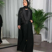 Woman wearing a black crepe blazer-style abaya with satin lapel and feather detailing on one shoulder.