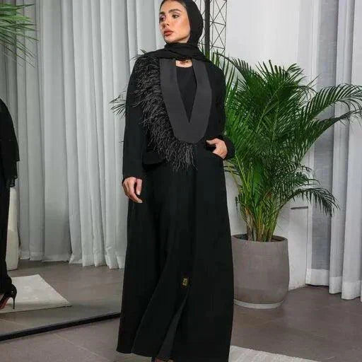 Woman wearing a black crepe blazer-style abaya with satin lapel and feather detailing on one shoulder.