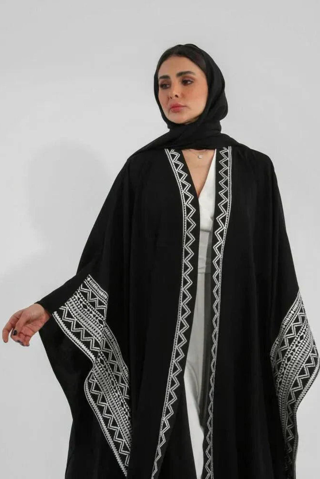 Woman wearing black crepe bisht with white Sadoo hand embroidery and open front design over white outfit