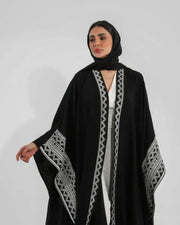 Woman wearing black crepe bisht with white Sadoo hand embroidery and open front design over white outfit