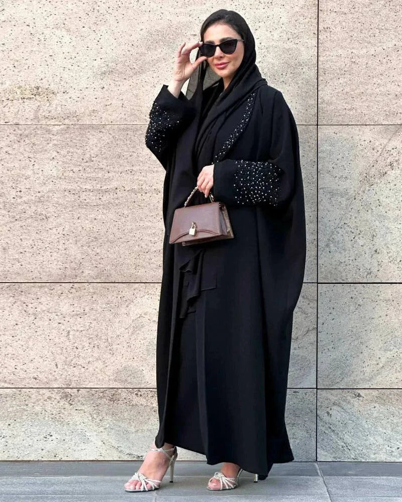 woman wearing black freesize blazer with black and silver hand embroidery on sleeves standing against stone wall carrying brown handbag