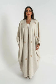 woman wearing beige linen bisht abaya with delicate hand embroidery and relaxed fit