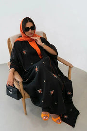 Black Obsidian bisht abaya with red and beige floral embroidery, orange piping, and relaxed fit worn with orange accessories