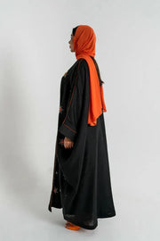 Black Obsidian bisht abaya with red and beige floral embroidery, orange piping, and relaxed fit worn with orange accessories