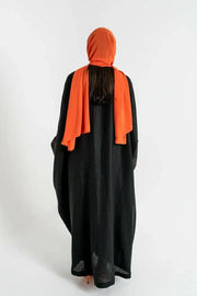 Black Obsidian bisht abaya with red and beige floral embroidery, orange piping, and relaxed fit worn with orange accessories