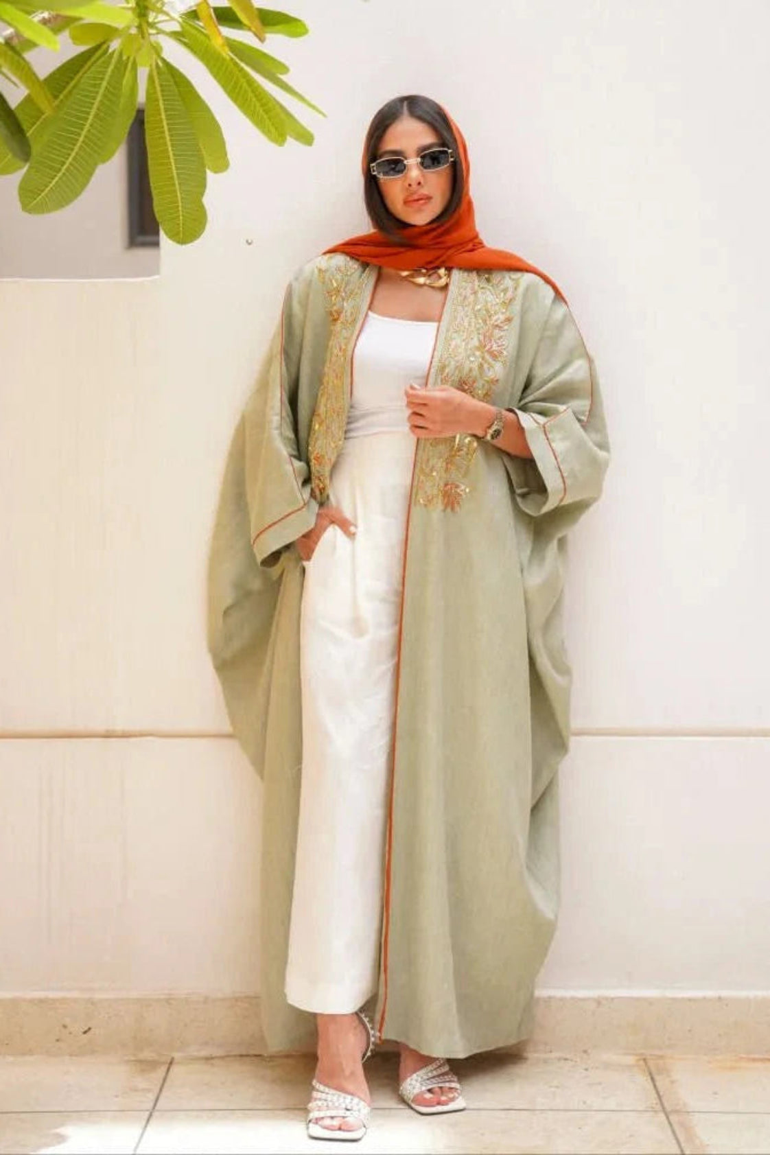 Light green pure linen abaya with hand embroidery in gold and orange tones, worn with white outfit and orange headscarf