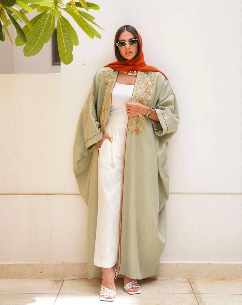 Light green pure linen abaya with hand embroidery in gold and orange tones, worn with white outfit and orange headscarf