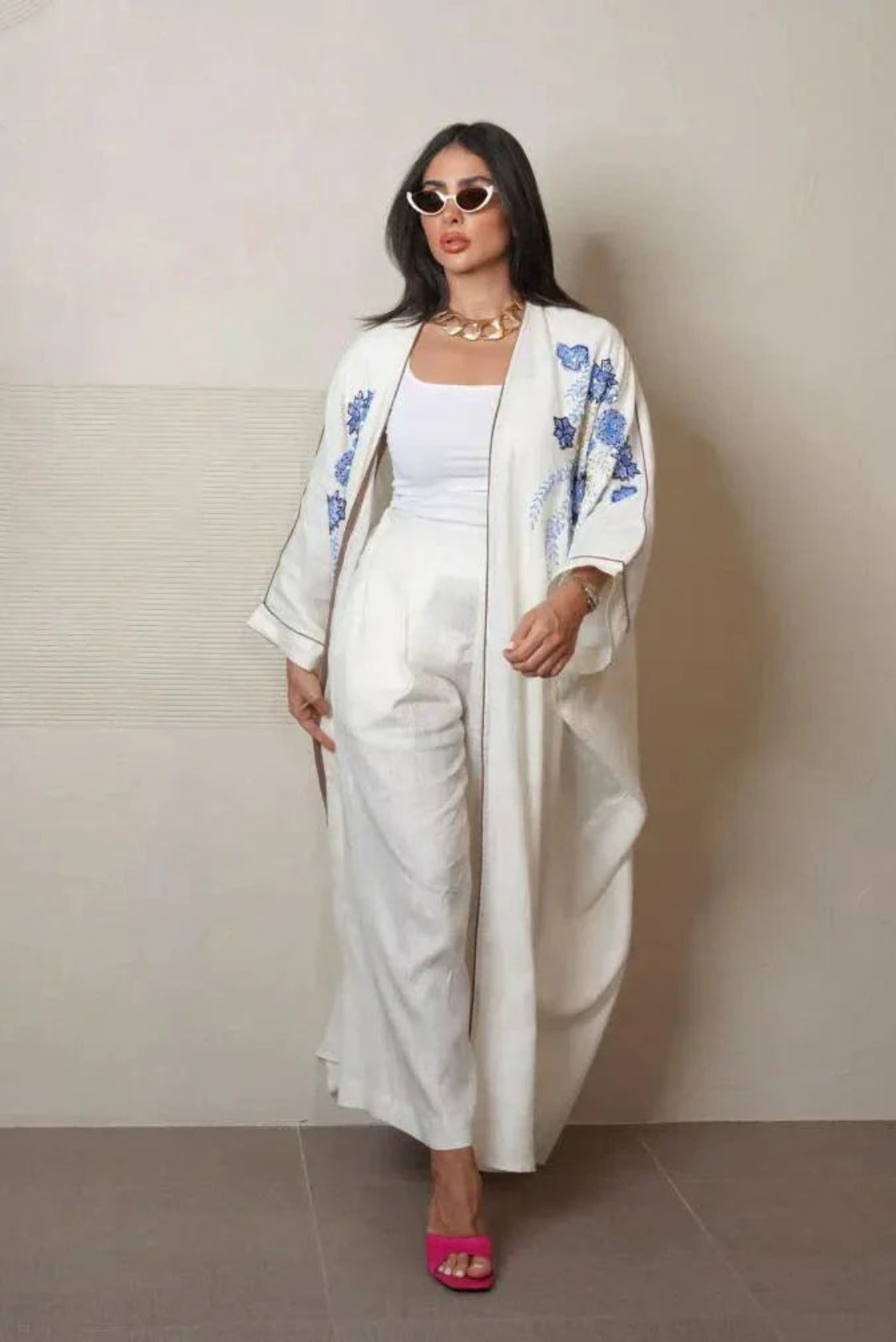 Elegant white abaya from linen with blue and gold hand embroidery, loose flowing silhouette, styled with white pants and pink heels