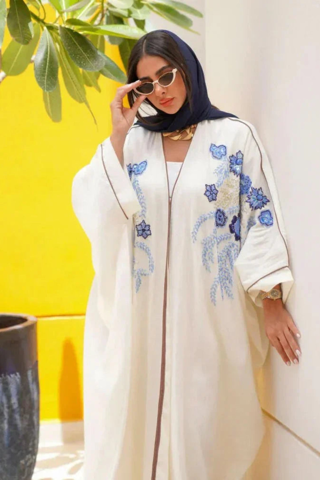 Elegant white abaya from linen with blue and gold hand embroidery, loose flowing silhouette, styled with white pants and pink heels