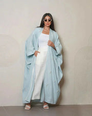 Woman wearing a sky-blue lightweight linen abaya with delicate white and crystal hand embroidery, styled with white sandals and sunglasses.