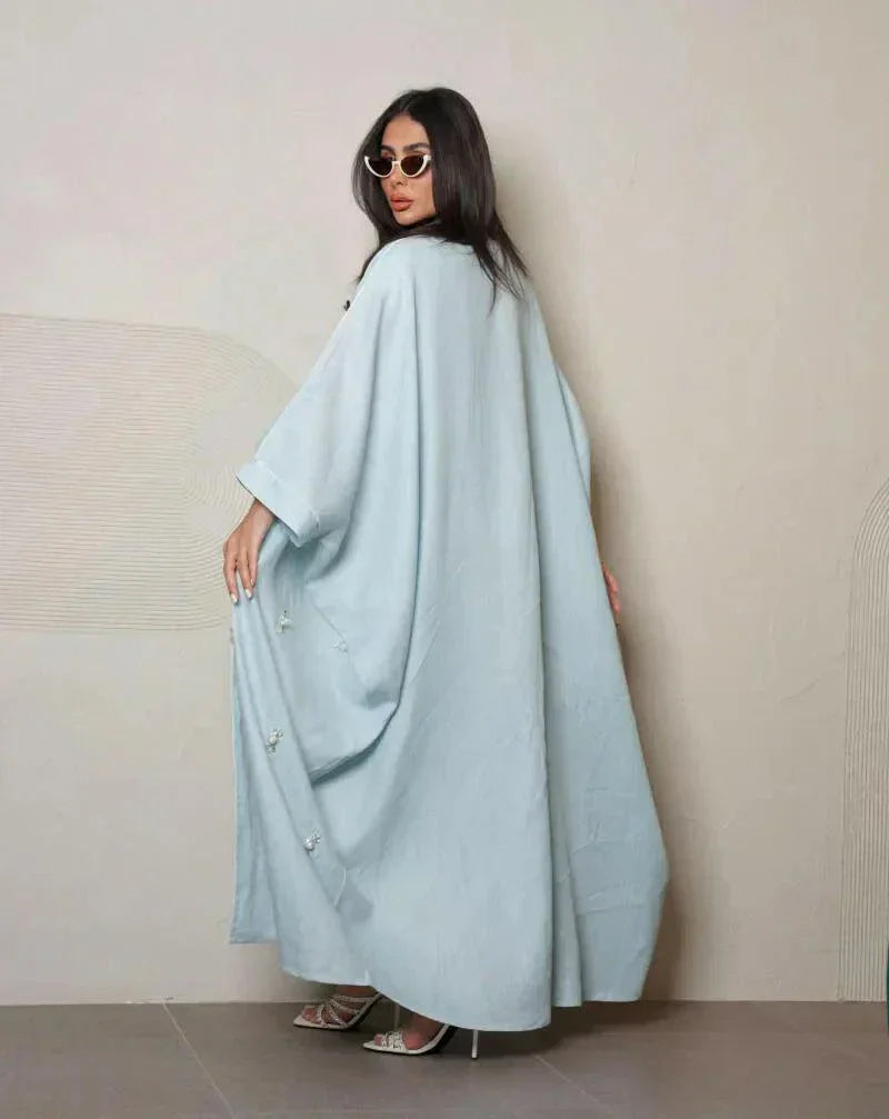 Woman wearing a sky-blue lightweight linen abaya with delicate white and crystal hand embroidery, styled with white sandals and sunglasses.