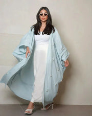 Woman wearing a sky-blue lightweight linen abaya with delicate white and crystal hand embroidery, styled with white sandals and sunglasses.