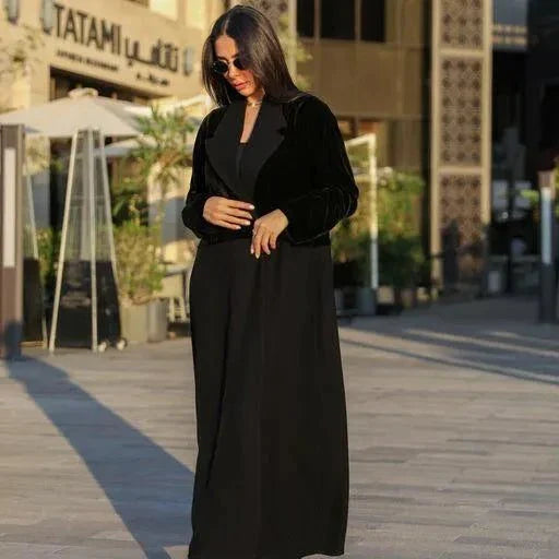 Woman wearing a chic black Velvet Noir blazer-style abaya with velvet panels and flowing crepe fabric outdoors.