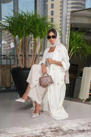 Elegant white linen abaya with gold and white hand-embroidered floral motifs, styled with matching hijab and accessories