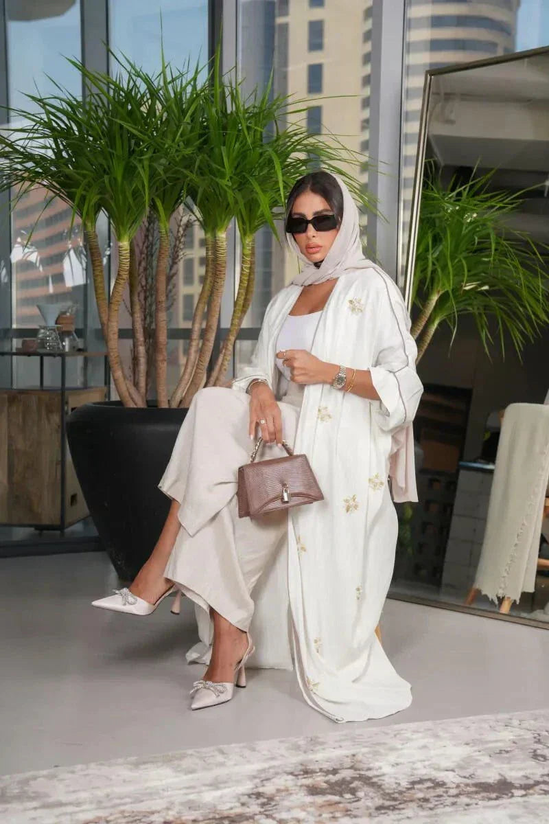 Elegant white linen abaya with gold and white hand-embroidered floral motifs, styled with matching hijab and accessories